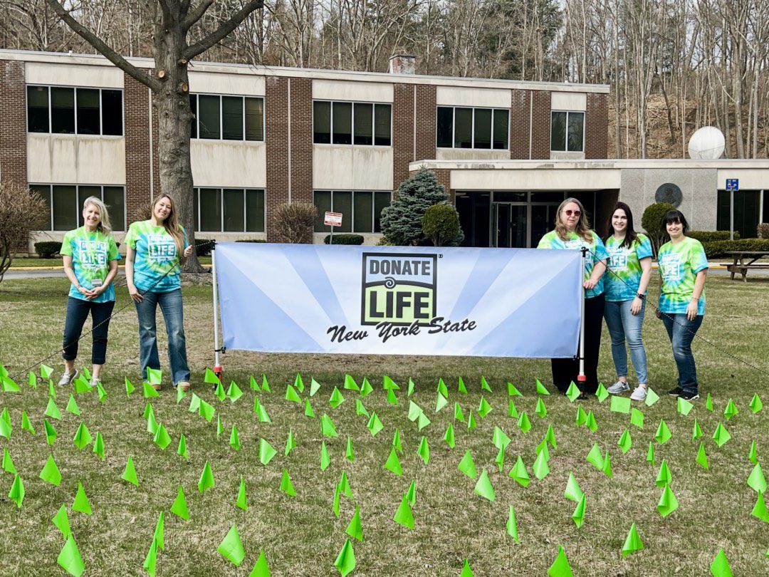 Montgomery County Clerk Brittany Kolbe and DMV staff stand behind 377 flags displayed in front of the Fonda DMV, each representing a New Yorker who lost their life while waiting for an organ transplant. The display is part of the County Clerk’s efforts to raise awareness during Donate Life Month and encourage residents to register as organ donors.